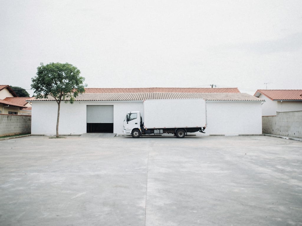 A quiet freight yard in Vila Izaura with a single parked white cargo truck and a pale depot building in soft morning light